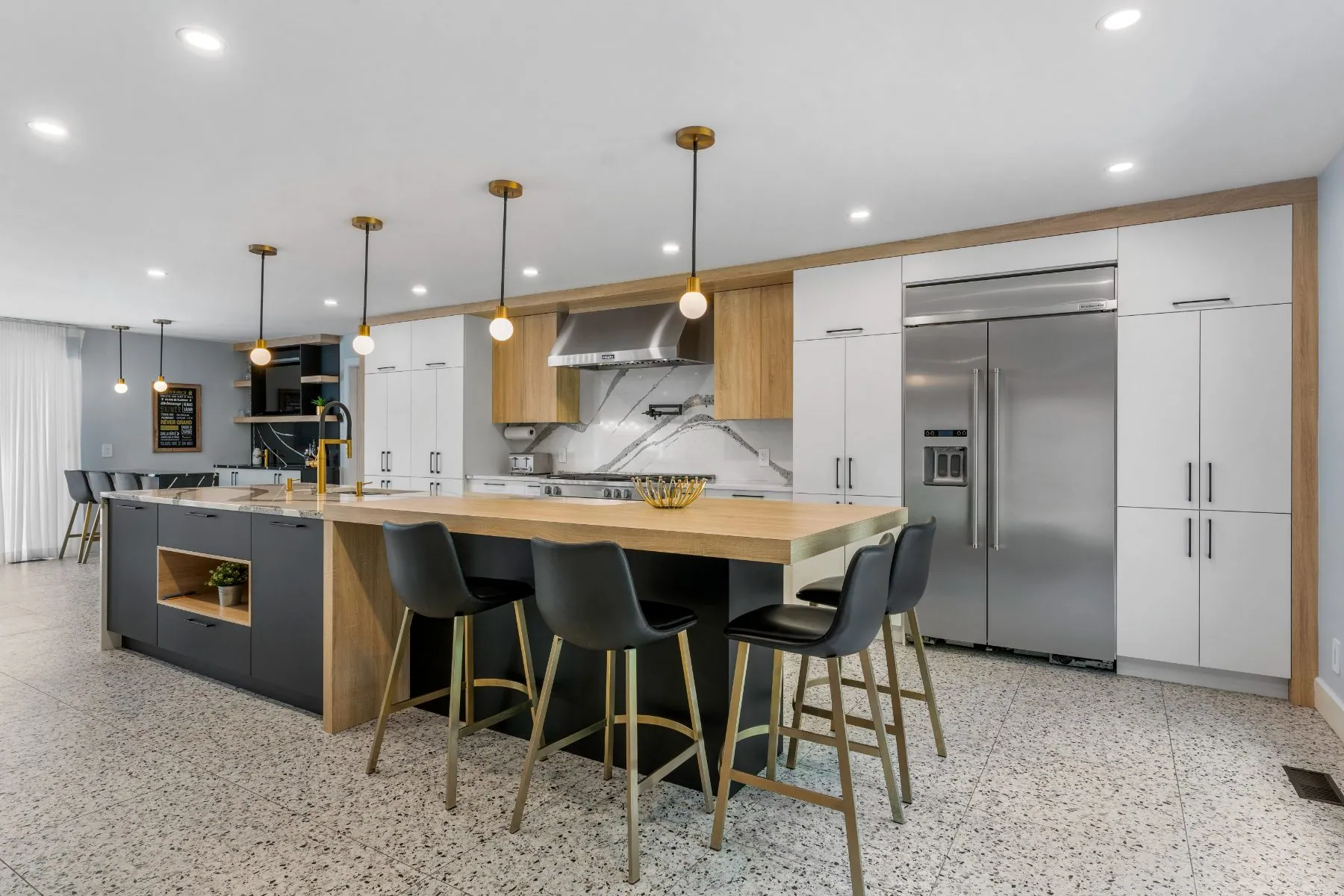 Kitchen with a long island, wood counter, brass pendants and terrazzo floor