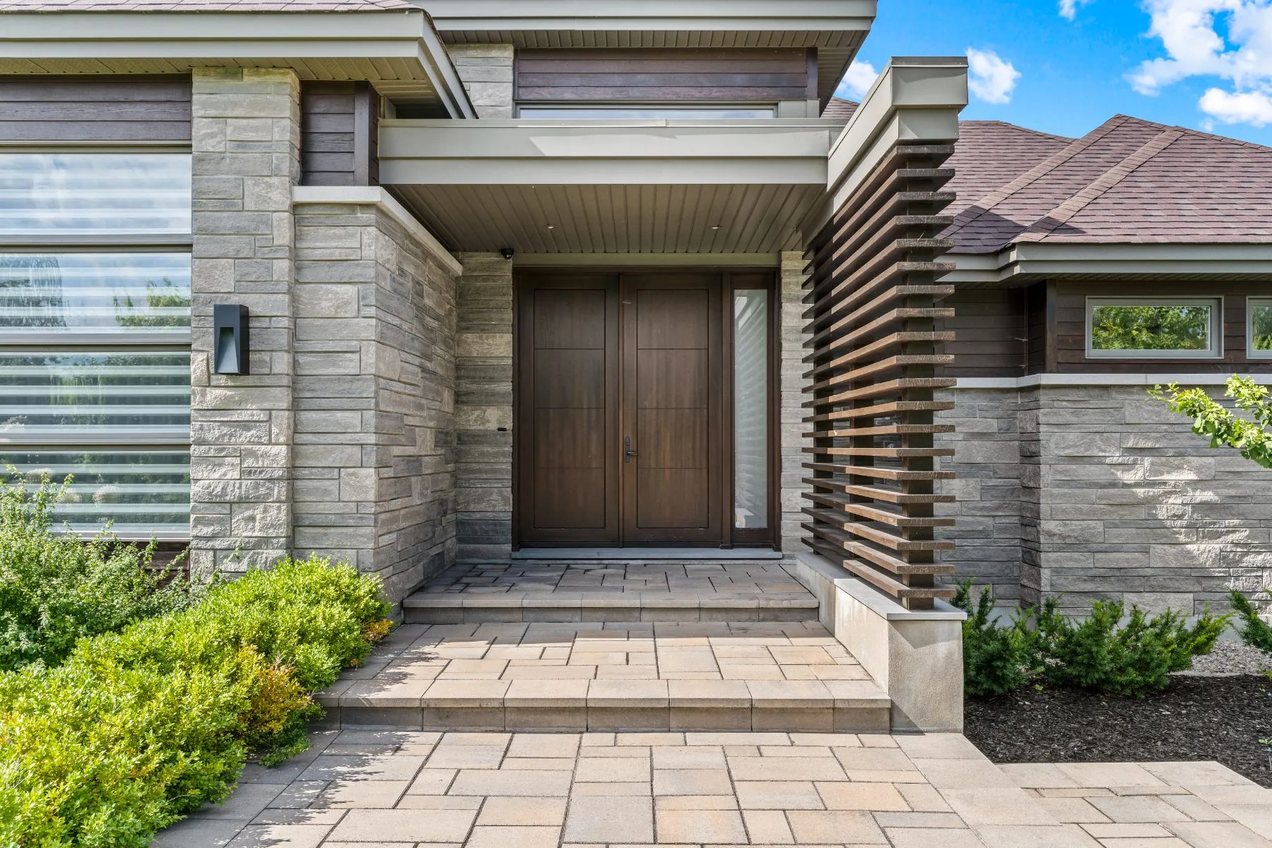 Entrance of a modern stone-and-wood home with double doors and a slatted wood screen